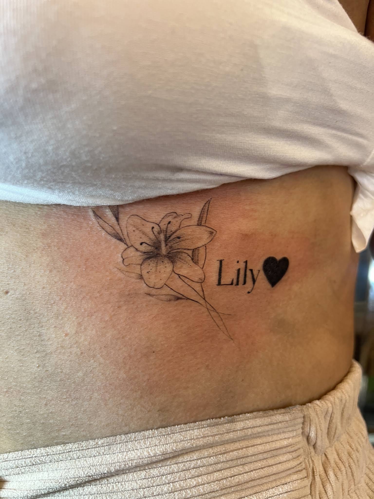 Fine line lily flower tattoo with name and heart on ribcage