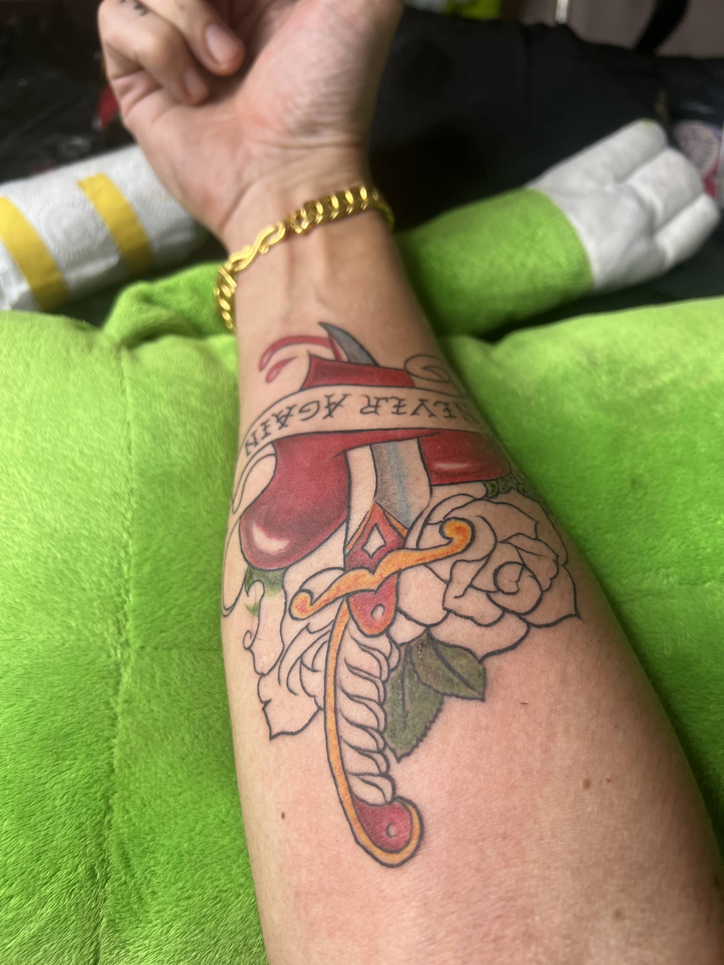 Traditional style dagger through heart with roses and scroll banner tattoo