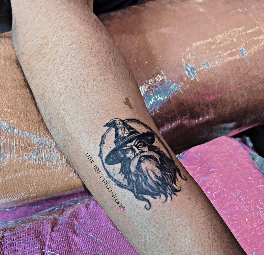 Black and grey illustrative wizard portrait tattoo on forearm
