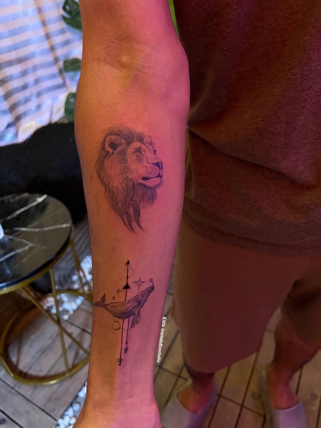 Realistic lion portrait with whale and compass geometric elements on forearm