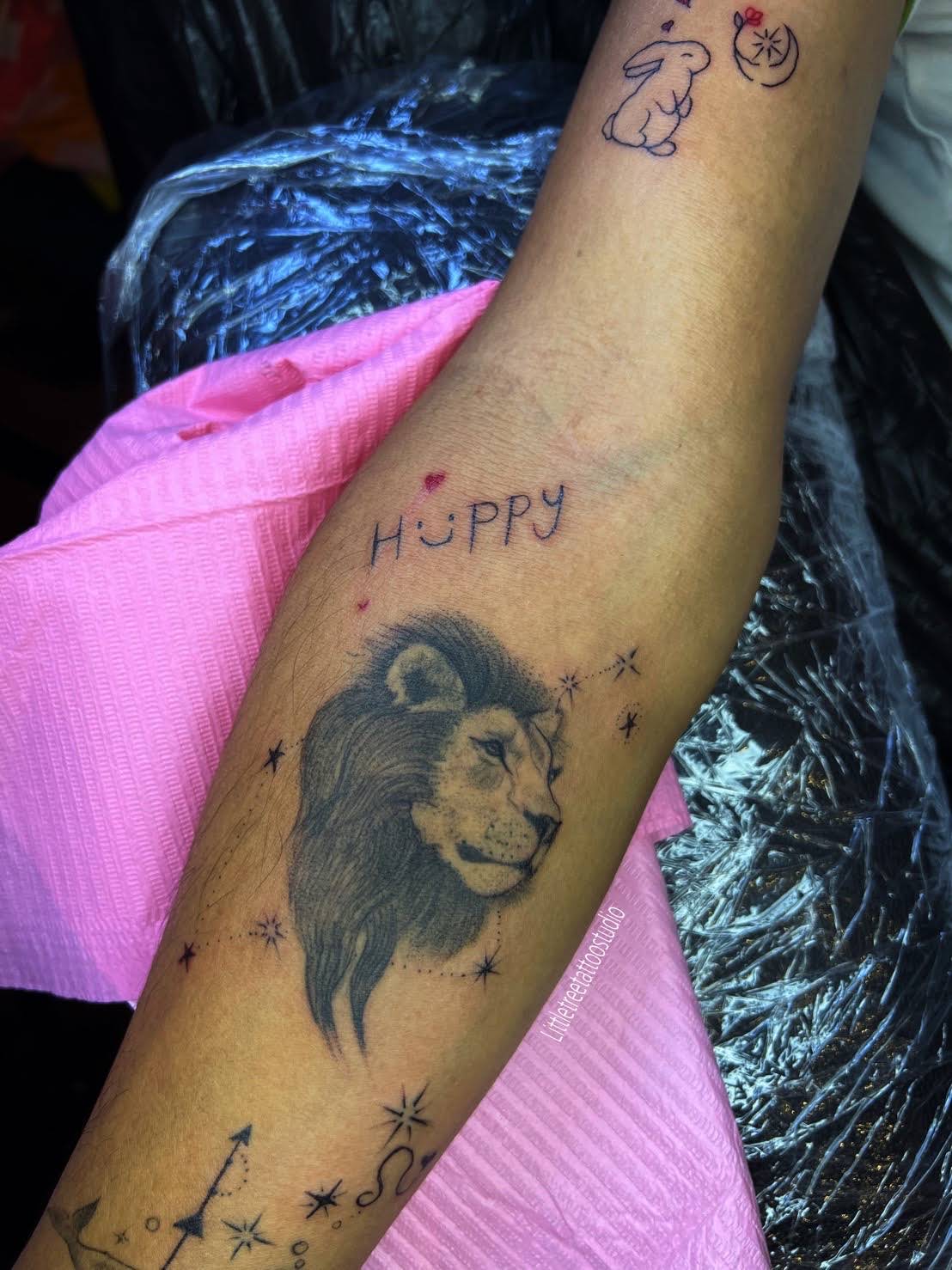 Realistic lion portrait with lettering, rabbit and constellation stars on forearm