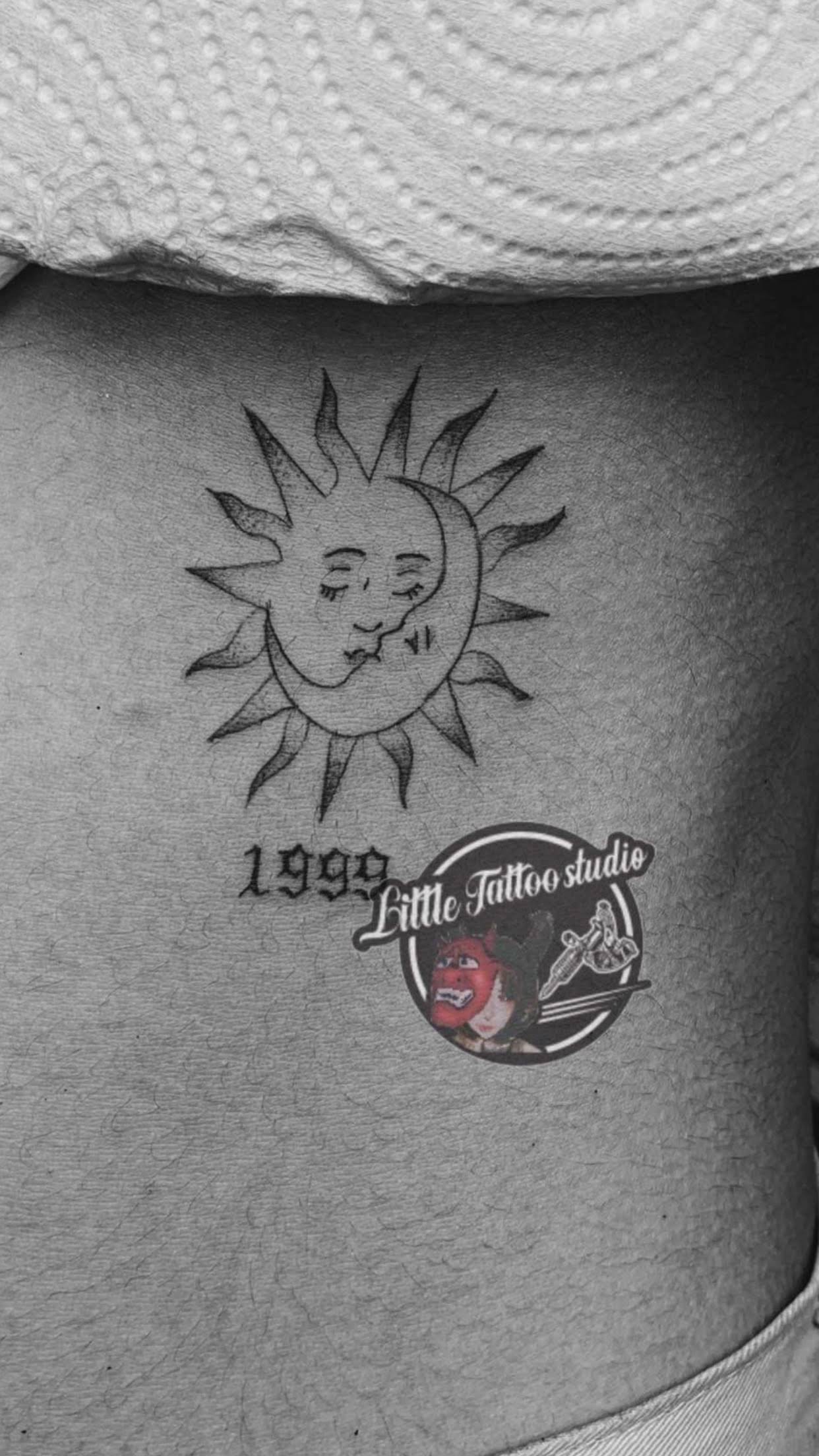 Black and grey celestial sun and moon faces with year tattoo on hip